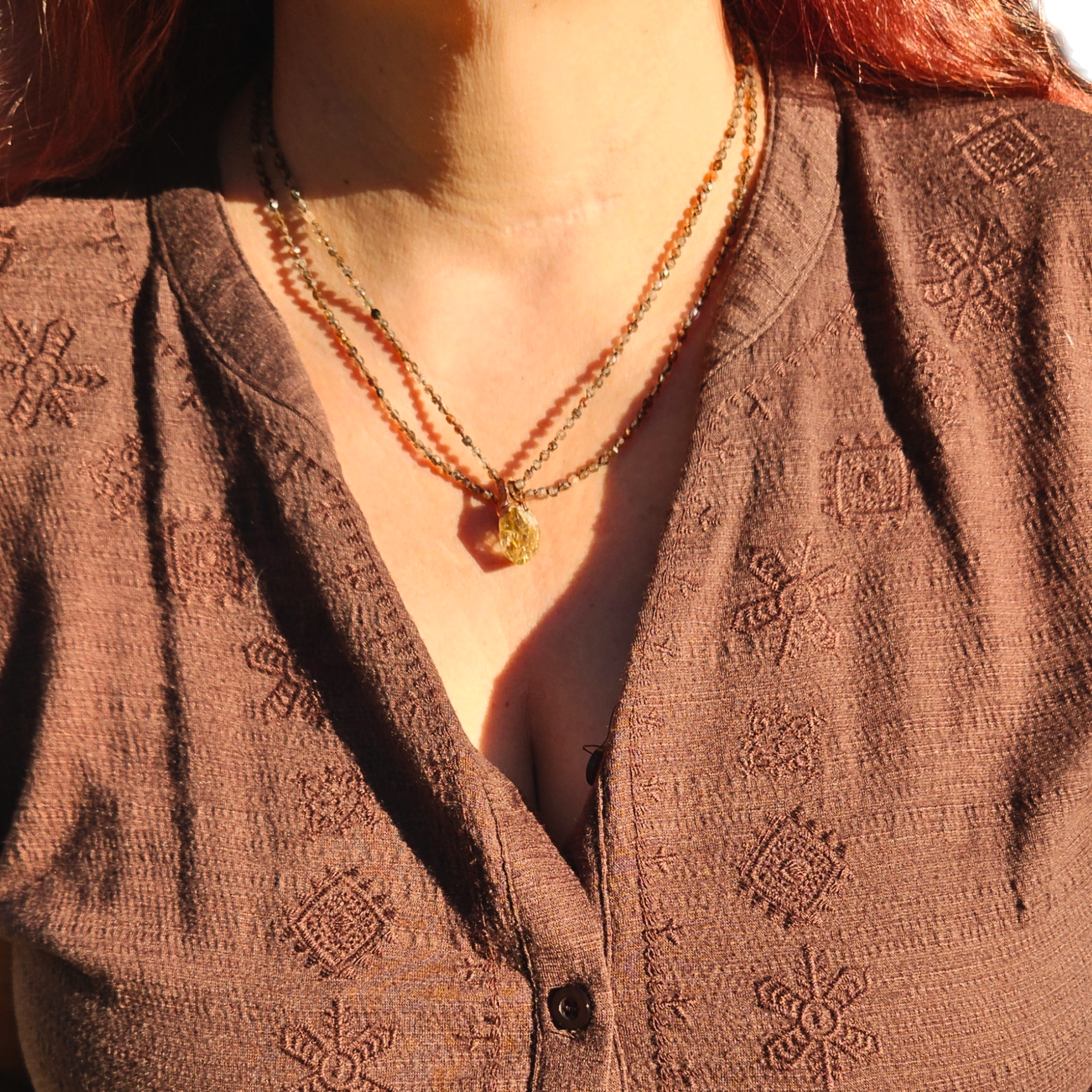 Model wearing the Earth's Veil Amulet with a double-layered Tunduru tourmaline bead strand resting over a earthy brown embroidered top.